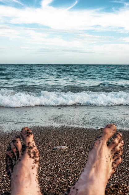 I piedi di un uomo sdraiato su una spiaggia sabbiosa vicino al mare