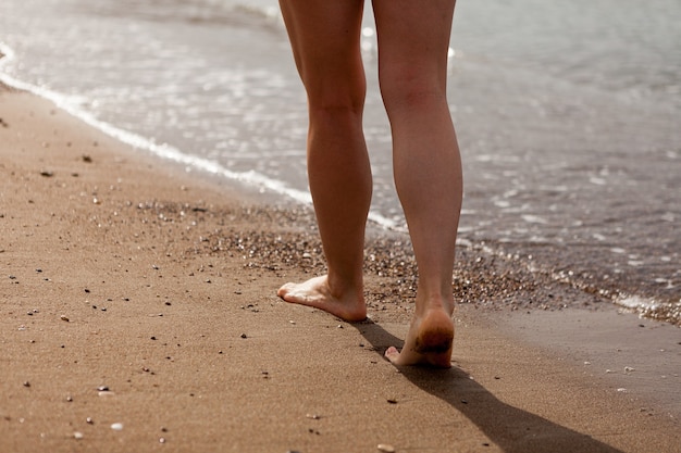 I piedi di una ragazza che camminano sulla sabbia lungo la sabbia della costa del mare e l'acqua di mare la ragazza cammina sul primo piano della fermata della sabbia