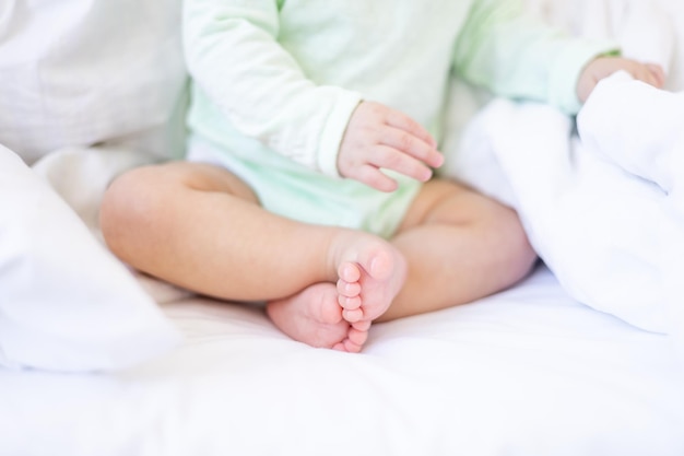 I piedi e le mani del bambino sul letto su un letto di cotone bianco, i tacchi rosa di un bambino piccolo