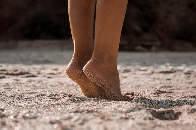 I piedi femminili stanno in punta di piedi su una spiaggia sabbiosa in una giornata estiva.