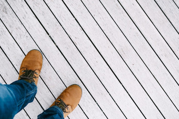 I piedi maschili in scarpe marroni stanno su un primo piano di legno bianco del pavimento