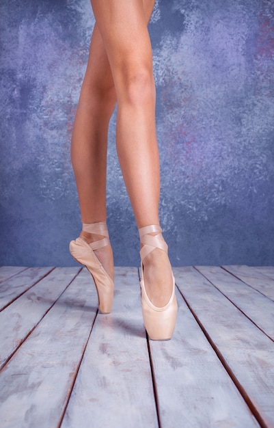 I piedi ravvicinati della giovane ballerina con le scarpe da punta sullo sfondo del pavimento in legno