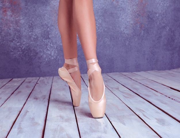 I piedi ravvicinati della giovane ballerina con le scarpe da punta sullo sfondo del pavimento in legno