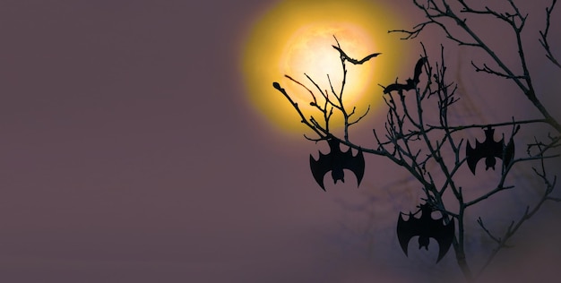 I pipistrelli di Halloween pendono dai rami degli alberi sullo sfondo di una luna piena