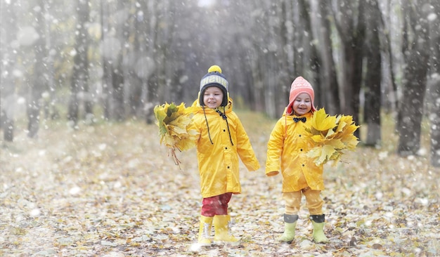 I più piccoli in una passeggiata nel parco autunnale. Primo gelo e prima neve nel bosco autunnale. I bambini giocano nel parco con neve e foglie.