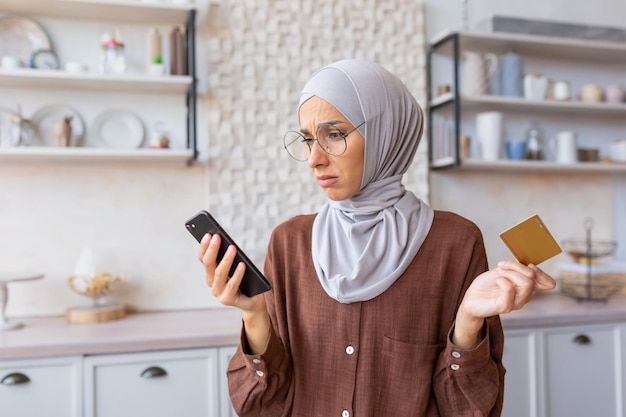 I problemi con il pagamento dell'acquisto dell'ordine online preoccupavano la giovane donna musulmana in hijab seduta in cucina