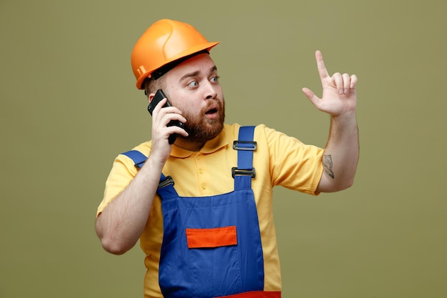 I punti impressionati in alto parlano al telefono giovane costruttore in uniforme isolato su sfondo verde