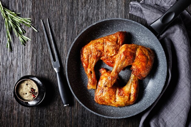 I quarti di coscia di pollo sono serviti su una padella con rametti di rosmarino fresco e pepe nero su uno sfondo di legno, vista dall'alto, primo piano