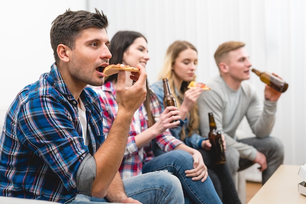 I quattro amici sul divano mangiano pizza e bevono una birra sullo sfondo bianco