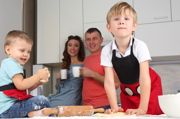 I ragazzini impastano la pasta sullo sfondo dei loro genitori