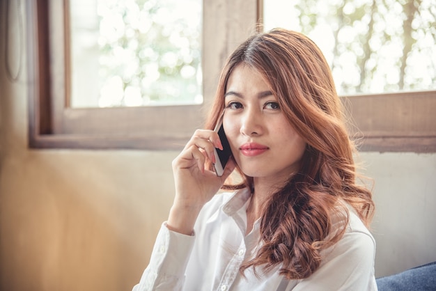 I ritratti di bella fiducia asiatica di sguardo della donna sono stanti e tenenti il ​​cellulare