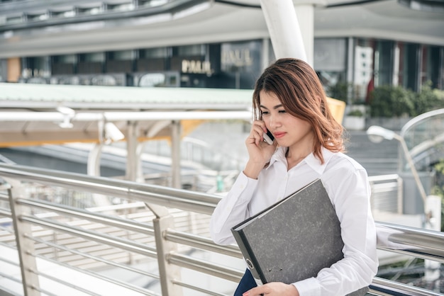 I ritratti di bella fiducia asiatica di sguardo della donna sono stanti e tenenti il cellulare