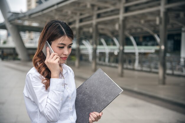 I ritratti di bella fiducia asiatica di sguardo della donna sono stanti e tenenti il cellulare