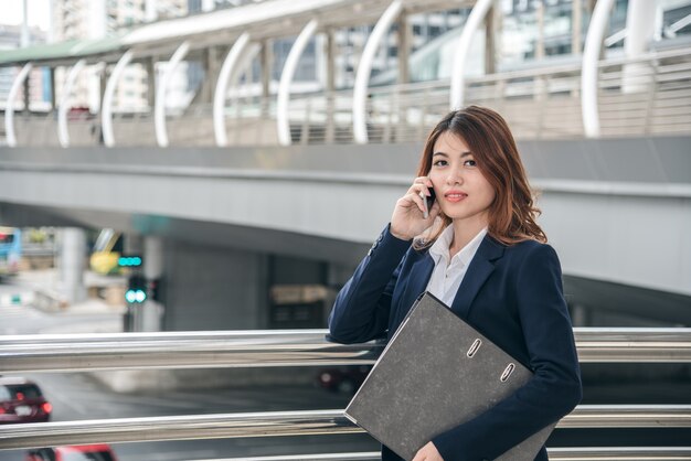 I ritratti di bella fiducia asiatica di sguardo della donna sono stanti e tenenti il cellulare
