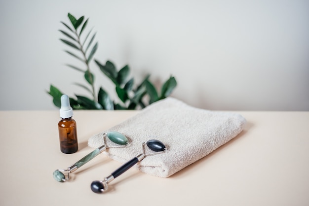 I rulli massaggianti Jade guasha sull'asciugamano e la bottiglia di siero spa rilassano il concetto di cura del viso e della pelle