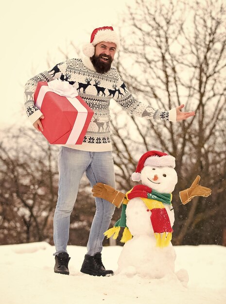 I sogni diventano realtà felice hipster pronto per le vacanze invernali di Natale maglione caldo quando fa freddo Babbo Natale regala presente uomo barbuto all'aperto costruire pupazzo di neve stagione invernale attività Buon Natale