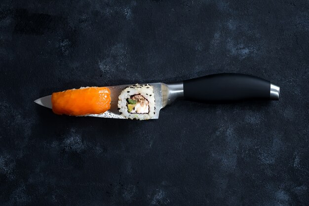 I sushi differenti sono servito su un coltello giapponese su una priorità bassa nera.