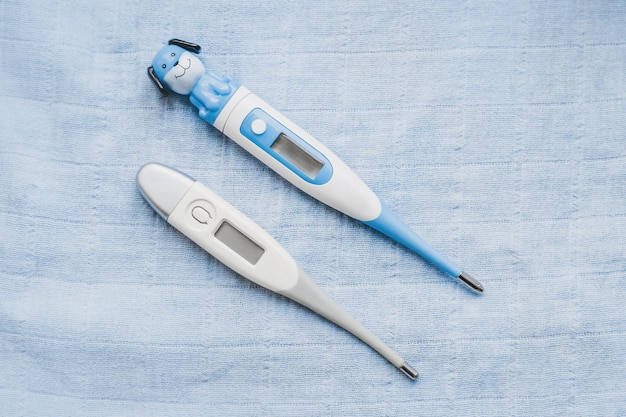 I termometri elettronici per bambini e adulti giacciono su uno sfondo medico blu
