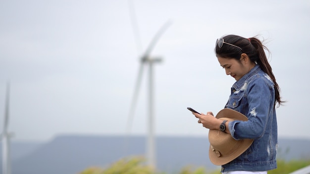 I turisti asiatici delle donne stanno prendendo un&#39;immagine di una turbina di vento in un punto scenico.
