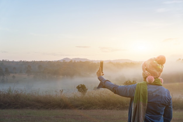 I turisti della donna prendono un'immagine con lo smartphone durante l'alba drammatica alla mattina nebbiosa dell'estate, concetto dell'avventura di campeggio all'aperto