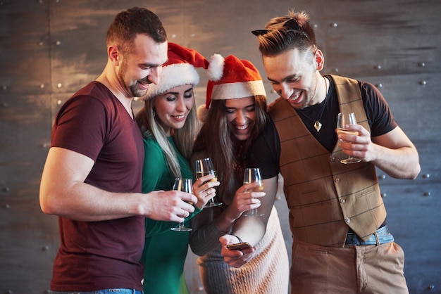 I vecchi amici allegri comunicano tra loro e guardano il telefono, con bicchieri di champagne nella festa di Capodanno. Concetto di intrattenimento e stile di vita. Wifi connesso persone