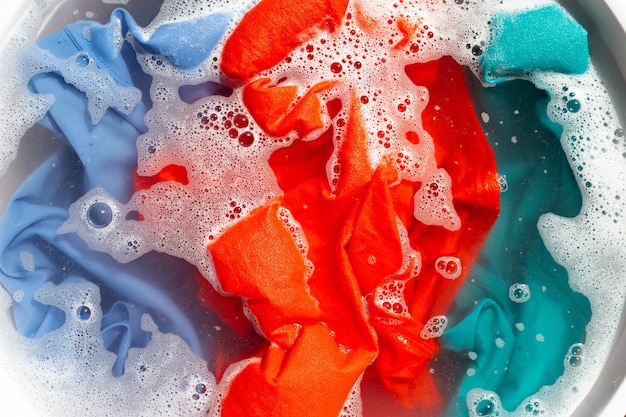 I vestiti colorati vengono immersi nella dissoluzione dell'acqua del detersivo in polvere Concetto di lavanderia