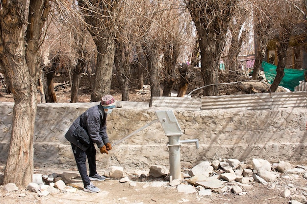 I viaggiatori tailandesi testano l'uso di antiche pompe a leva manuali per pozzi sotterranei all'aperto nel vicolo del villaggio di Ladakh nella valle himalayana nel Jammu e Kashmir India durante la stagione invernale