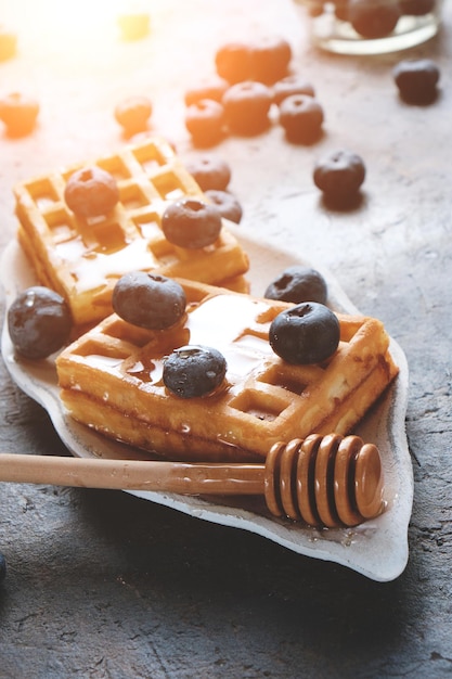 I waffle sono disposti su un piatto, decorati con mirtilli, cosparsi di miele dal cucchiaio di miele.