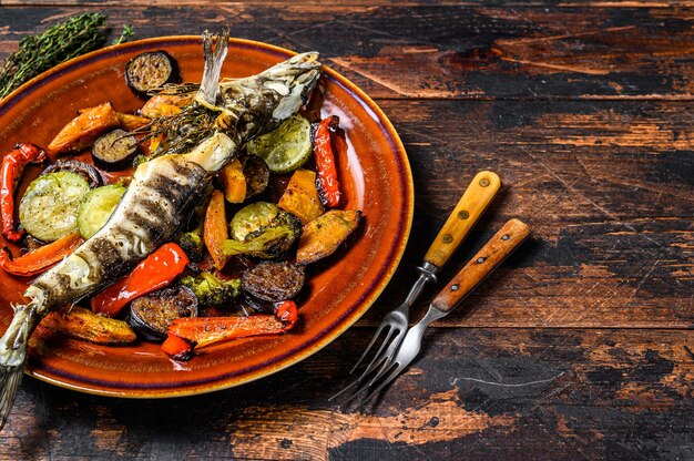 Icefish intero al forno con verdure grigliate. Sfondo in legno scuro. Vista dall'alto. Copia spazio.