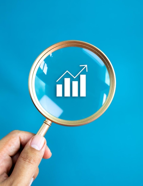 Icona del grafico di crescita del grafico analitico aziendale nella lente rotonda della lente d'ingrandimento in oro di lusso nella mano dell'uomo d'affari isolata su sfondo blu Tendenze alla ricerca di concetti di investimento di analisi azionaria del denaro