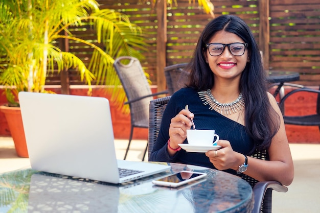 Idea per la pausa caffè. Giovane donna d'affari indiana che utilizza il computer tablet nel caffè del giardino estivo