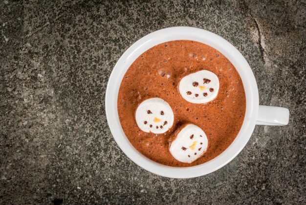 Idea tradizionale per un drink di Natale. Tazza di cioccolata calda con marshmallow, decorata a forma di pupazzi di neve, su pietra nera vista da tavolo