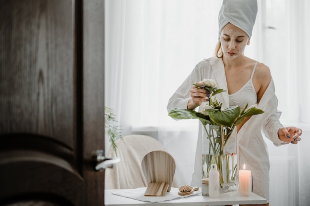 Idee per la cura di sé per la donna. La giovane donna in asciugamano che si raffredda in camera da letto e fa la routine di cura di sé di bellezza.