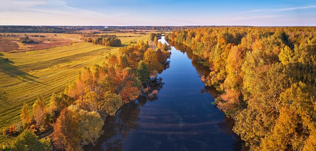 Idilliaco paesaggio autunnale soleggiato, scena aerea rurale - Foto stock. Alberi colorati di caduta che si riflettono nell'acqua, sfondo pittoresco. Foresta selvaggia, fiume, panorama al tramonto sul prato, Bielorussia