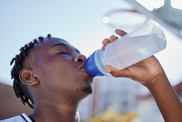 Idratazione dell'acqua e stile di vita sano di un uomo di colore sportivo che beve acqua da una bottiglia gustando una bevanda rinfrescante L'atleta africano ripristina gli elettroliti pur essendo attivo e si esercita all'aperto