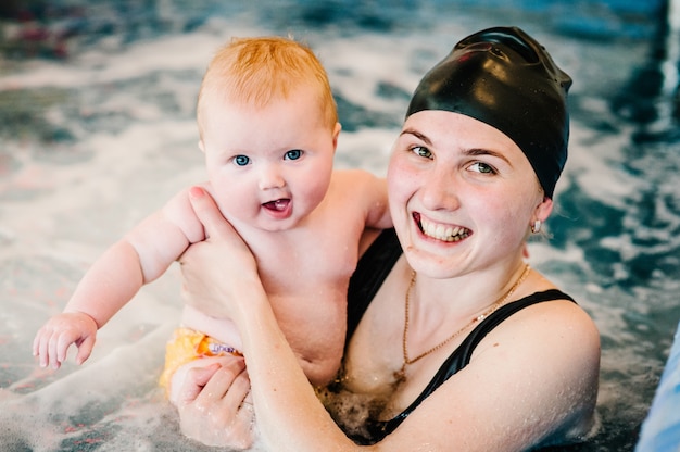 Idromassaggio, idromassaggio. Immersione bambino nella piscina per bambini. Giovane madre, istruttrice di nuoto e bambina felice in piscina. Impara il bambino a nuotare.