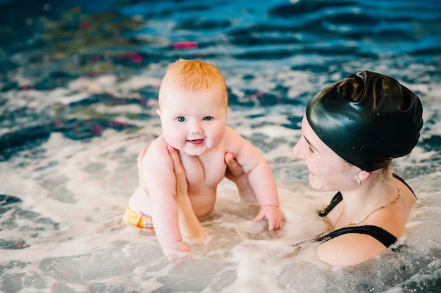 Idromassaggio, Immersione bambino nella piscina per bambini. Giovane madre, istruttrice di nuoto e bambina felice in piscina. Impara il bambino a nuotare. Goditi il primo giorno di nuoto in acqua.