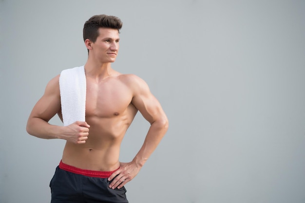 Igiene e concetto di salute. Atleta con braccia forti, bicipiti e tricipiti. Sportivo con asciugamano sul collo su sfondo grigio. Forma fisica e sport. Uomo con torso nudo con confezione da sei e ab, copia spazio