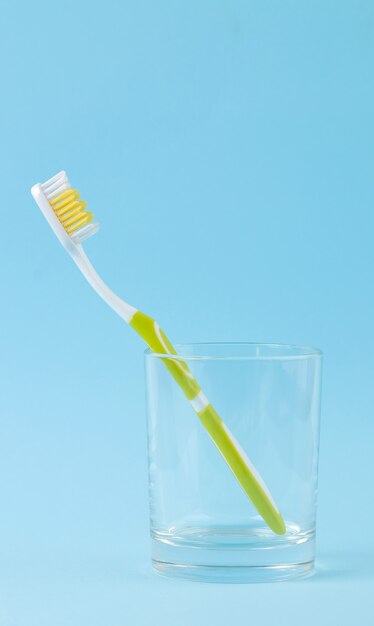 Igiene orale. spazzolino da denti verde in un bicchiere su un blu delicato.