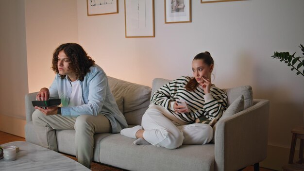 Ignorando la coppia seduta a casa sul divano sconvolta donna che cerca smartphone marito che mangia