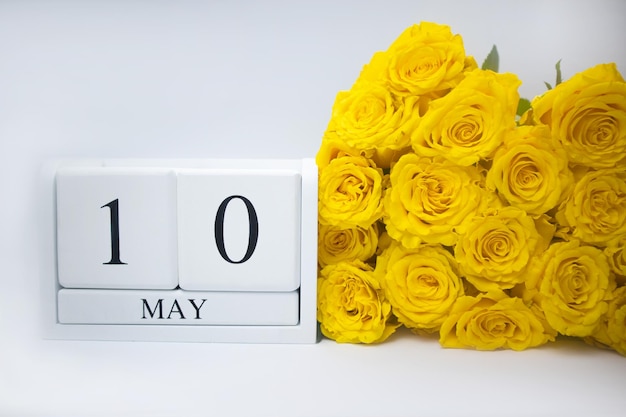 Il 10 maggio su un calendario di legno bianco e un mazzo di rose gialle si trovano fianco a fianco
