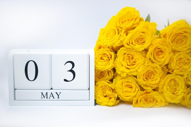 Il 3 maggio su un calendario di legno bianco e un mazzo di rose gialle si trovano fianco a fianco