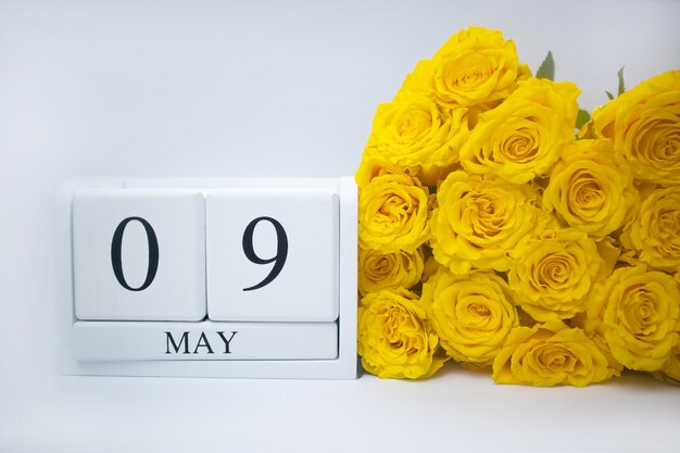 Il 9 maggio su un calendario di legno bianco e un mazzo di rose gialle si trovano fianco a fianco