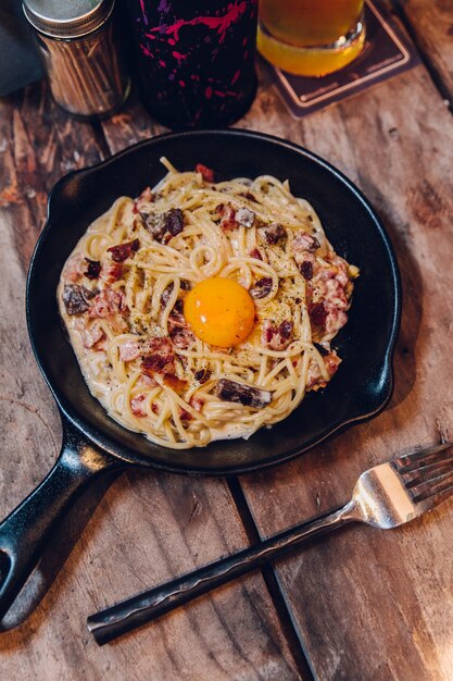 Il bacon del tuorlo di Carbonara del Fettuccine è servito in pentola nera sulla tavola di legno.