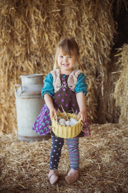 Il bambino affascinante raccoglie le uova di gallina in un cesto in un fienile