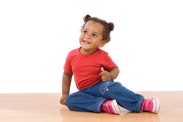 Il bambino africano adorabile si siede sopra il pavimento di legno