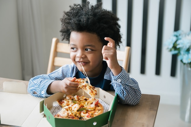 Il bambino afroamericano felice mangia la pizza sul tavolo