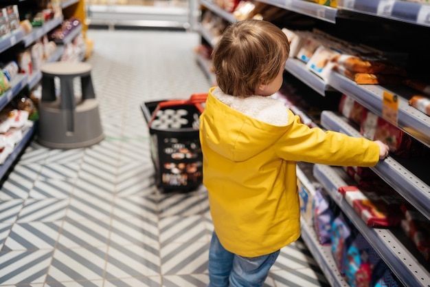 Il bambino al mercato con un carrello della spesa sceglie una vista posteriore del prodotto