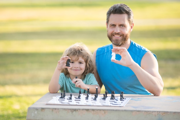 Il bambino all'aperto della famiglia felice gioca a scacchi padre e figlio che giocano a scacchi nel giardino di primavera