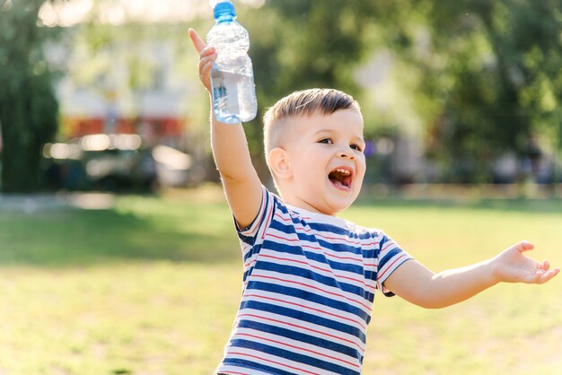 Il bambino allegro beve l'acqua libera da una bottiglia un giorno soleggiato in natura